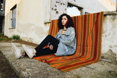 Free Woman Wearing Denim Jacket Sitting on Striped Blanket Stock Photo