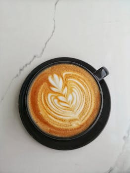 Aerial shot of a latte with intricate latte art served in a black saucer on a marble surface.