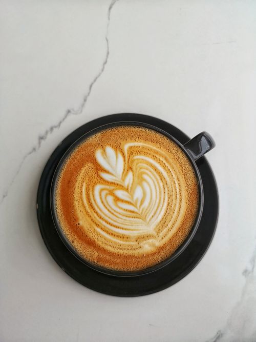 Free Aerial shot of a latte with intricate latte art served in a black saucer on a marble surface. Stock Photo