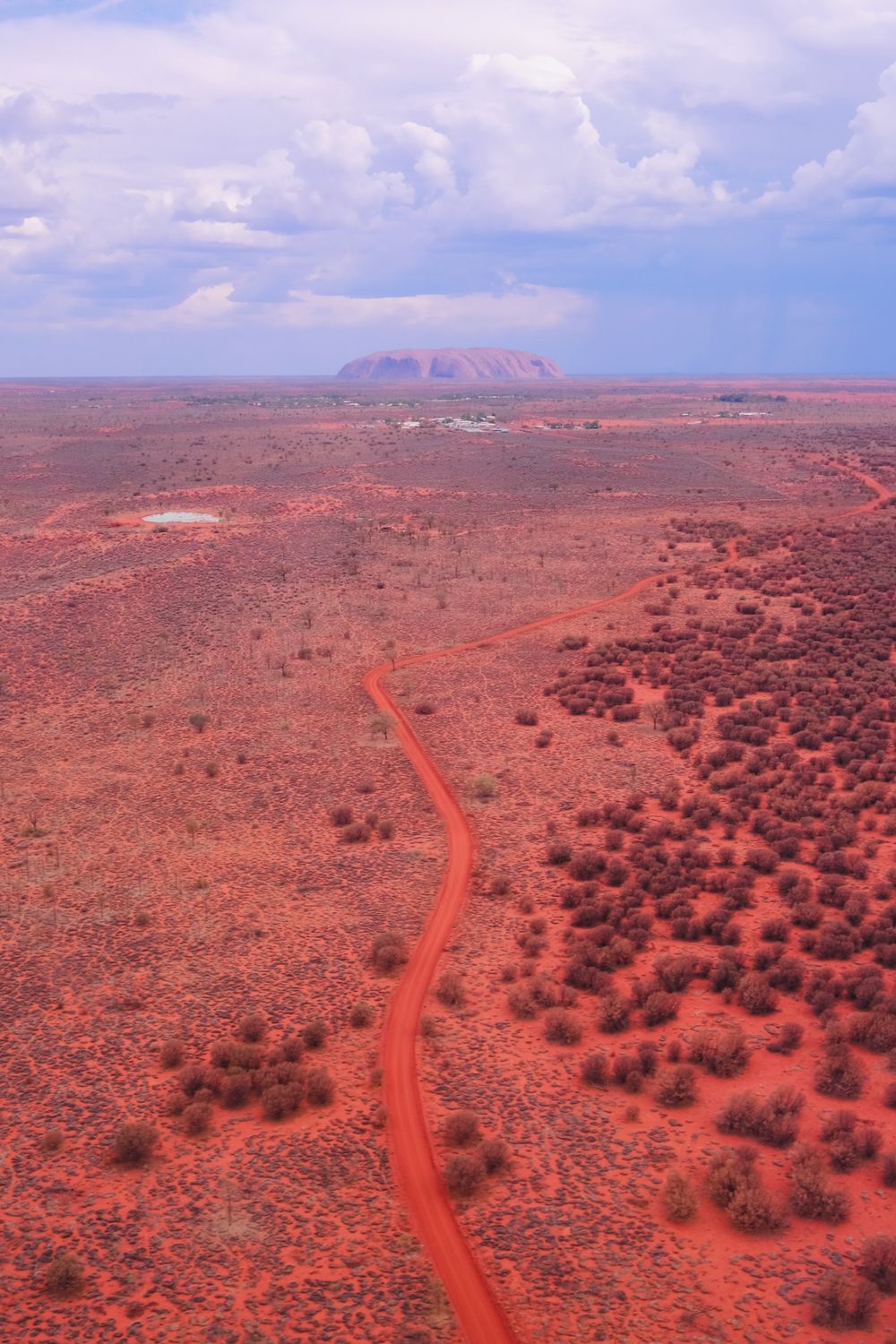 Camino rojo serpenteando por el Outback con Uluru en el horizonte