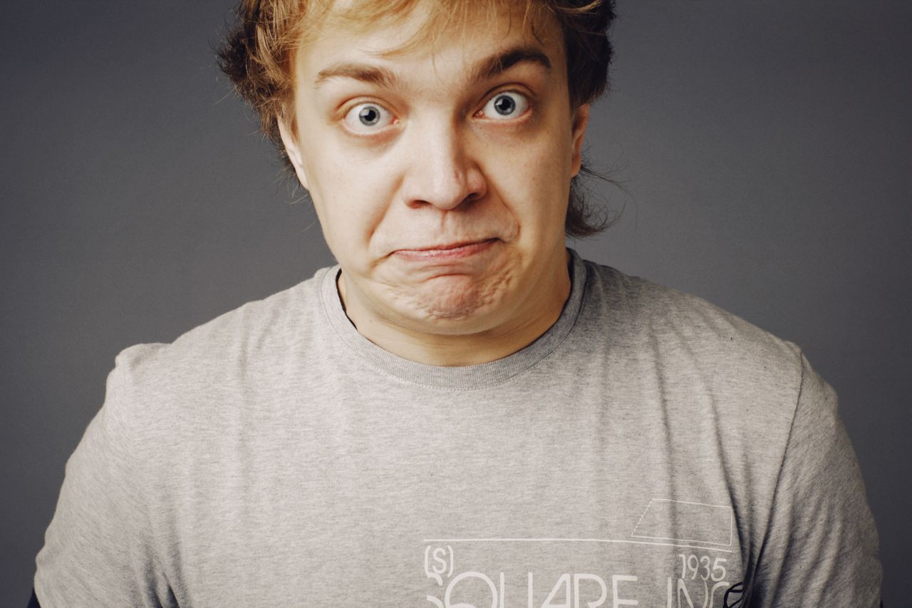close up portrait of a young man in a gray t shirt making a humorous f