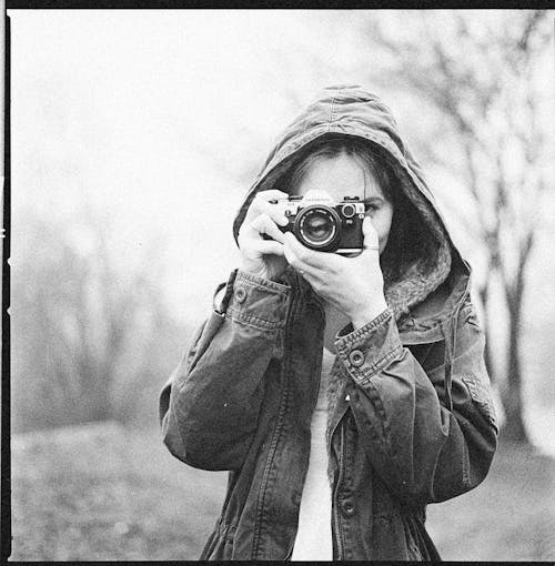 Grayscale Photo of Woman Wearing Hoodie Jacket Holding Camera