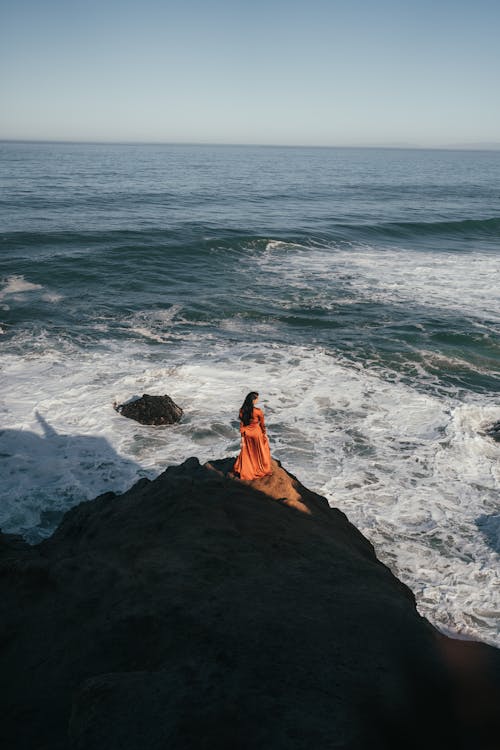 High Angle View of Woman in Long Brown Dress Standing on Rocky Coast
