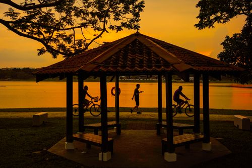 Free Silhouetted people at a lakeside gazebo during sunset in Singapore, capturing tranquility. Stock Photo
