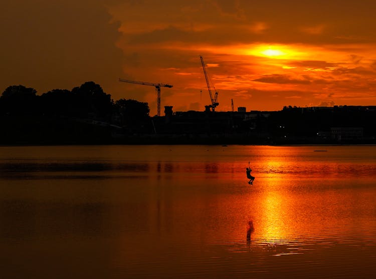 Silhouette Of Person Riding A Zipline Over The Lake