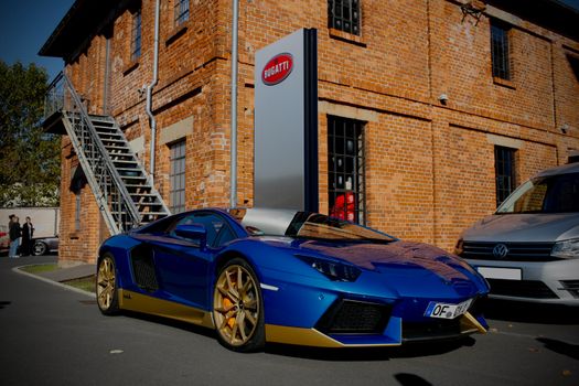 Blue luxury sports car parked outside a historic brick building under bright daylight.