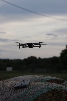 Aerial drone hovering above straw bales in a field under a dusky sky, showcasing modern technology in nature.