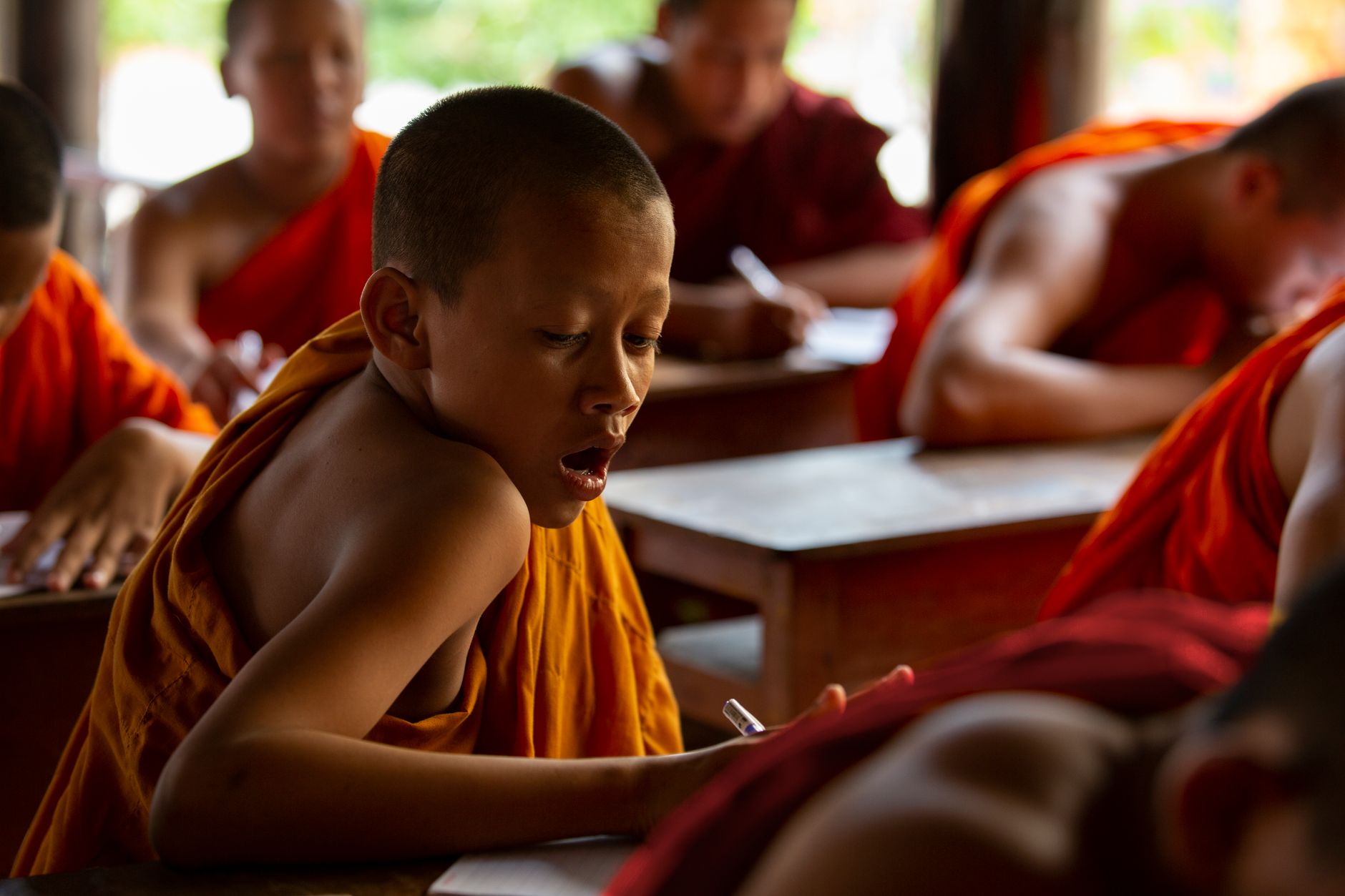 Young monks participate in a classroom setting, focusing on their studies in traditional robes.