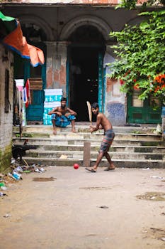 Two young men play street cricket on a vibrant urban street, showcasing recreation and cultural sports.