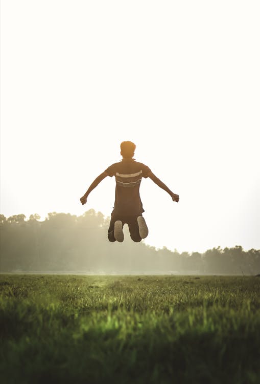 Man Wearing Polo Shirt Jumping on Green Grass Field