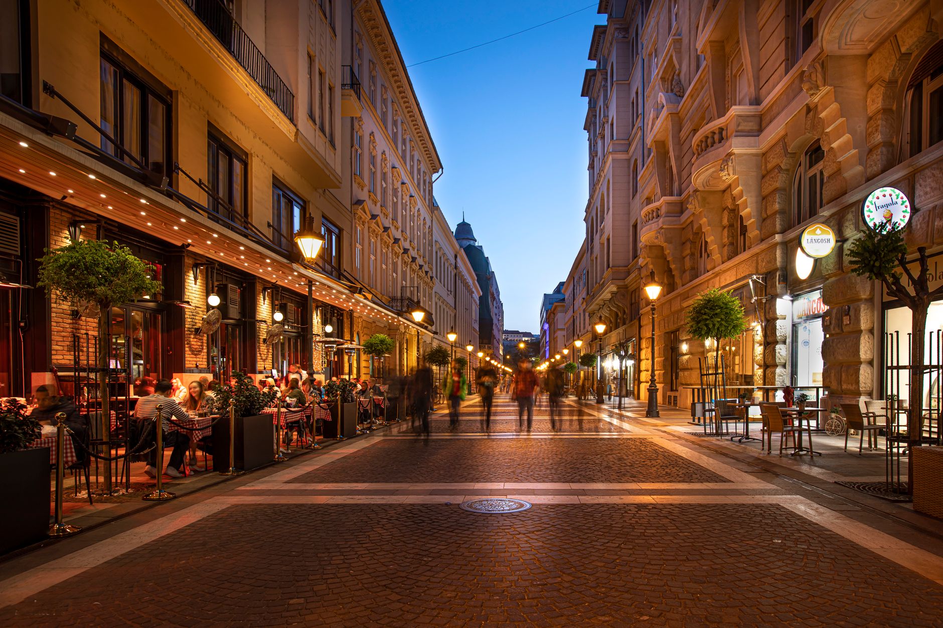 Bustling street at night with people enjoying outdoor cafes and lit buildings.
