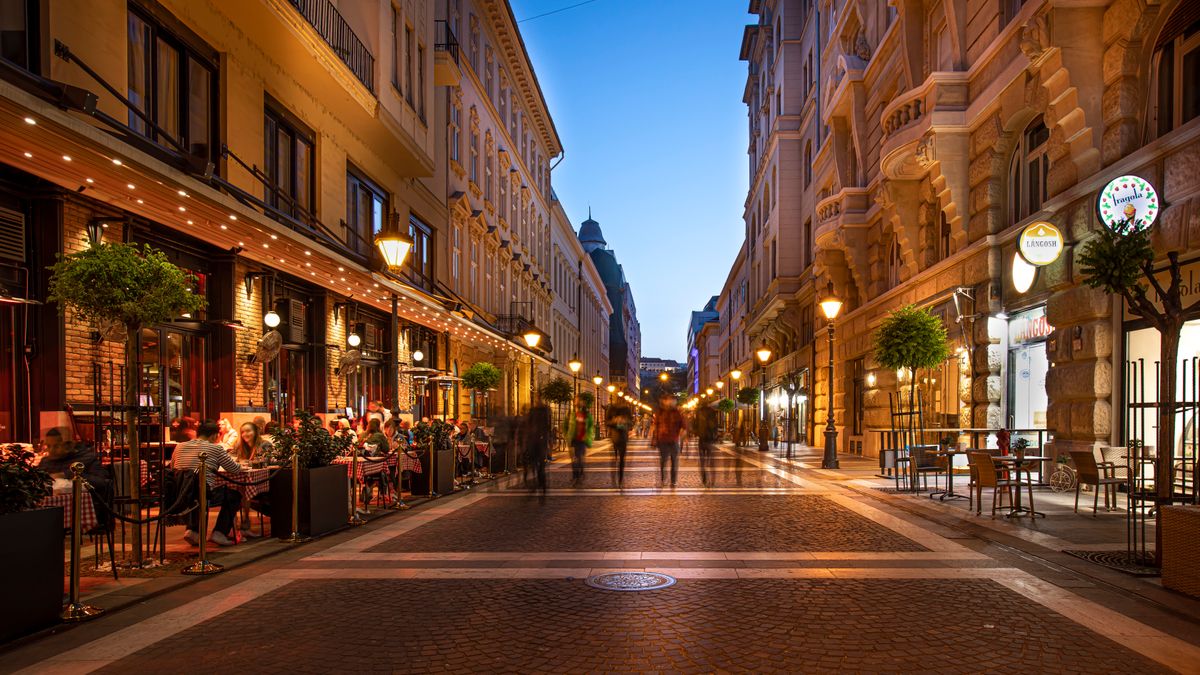 Bustling street at night with people enjoying outdoor cafes and lit buildings.