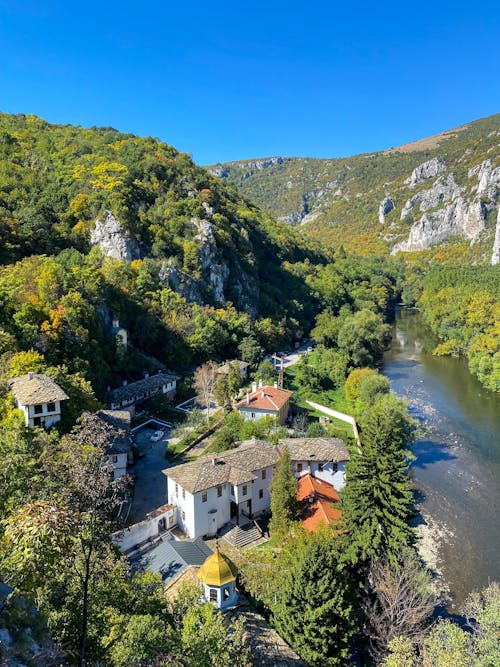 Houses Near a River Between Green Rocky Mountains