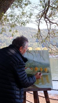 A man painting a serene landscape by the lake during autumn in Bozdağ, İzmir.