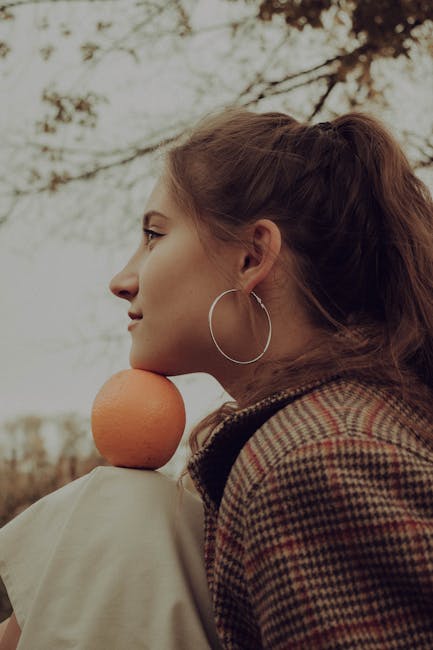 Side profile of a woman holding an orange under her chin outdoors with autumn vibes. Unique portrait style.