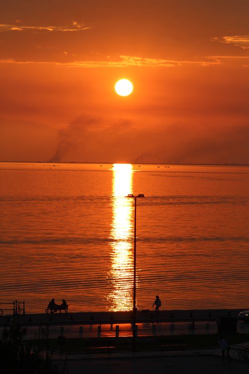 Free A vibrant sunset over the Aegean Sea in Thessaloniki, Greece, with silhouettes on the boardwalk. Stock Photo