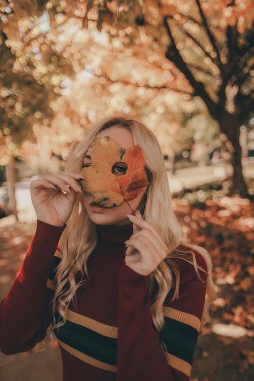 Woman Looking through Hole in Autumn Leaf in Park
