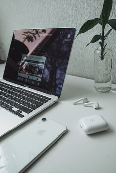 Clean and organized workspace featuring a laptop, smartphone, and earbuds on a white desk.