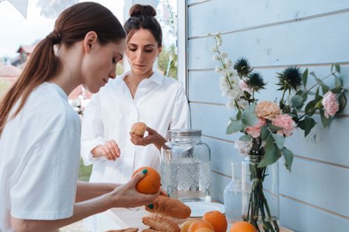 Free Two women arranging bread and flowers on a table outdoors, creating a serene setting. Stock Photo