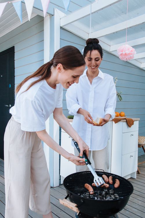 Free Two women enjoy grilling sausages outdoors during a cheerful summer BBQ party. Stock Photo