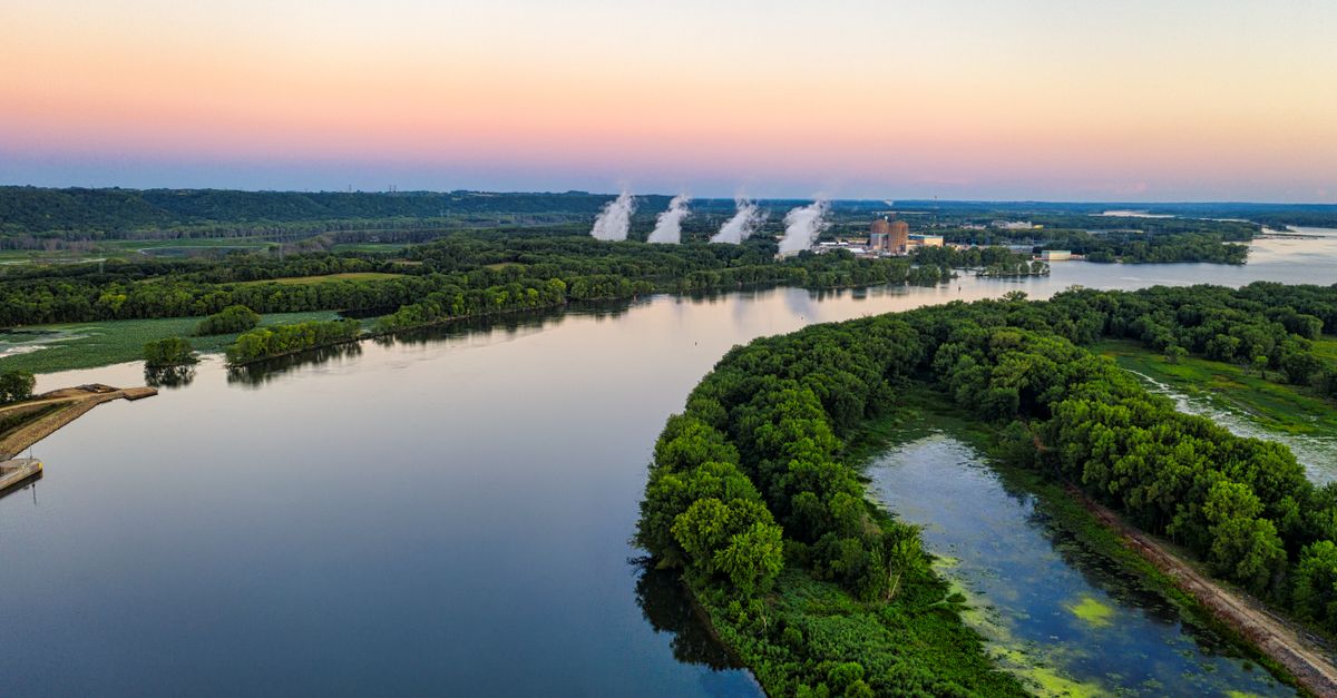 Aerial shot of the Mississippi River with lush greenery and distant smoke at dusk, near Welch, MN.