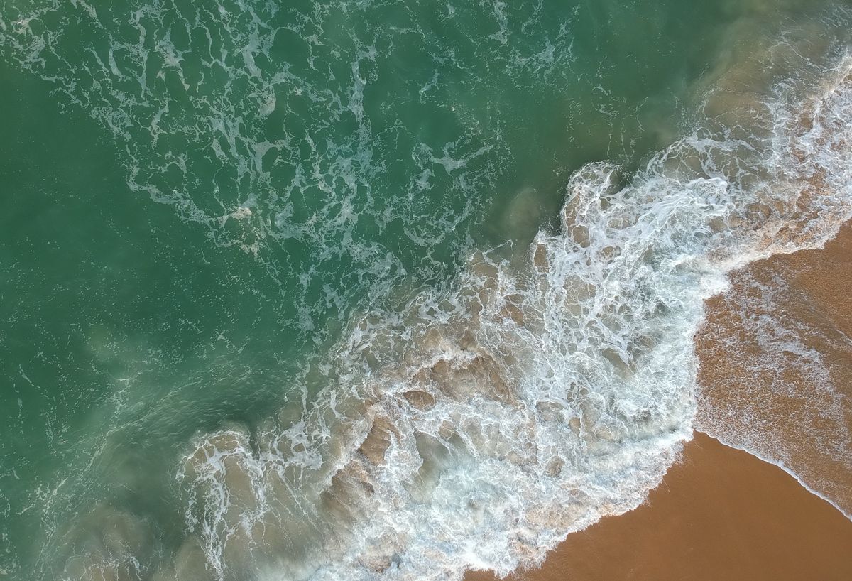 Aerial view of a beach showing waves breaking in different sections, surfers in the water and white sand