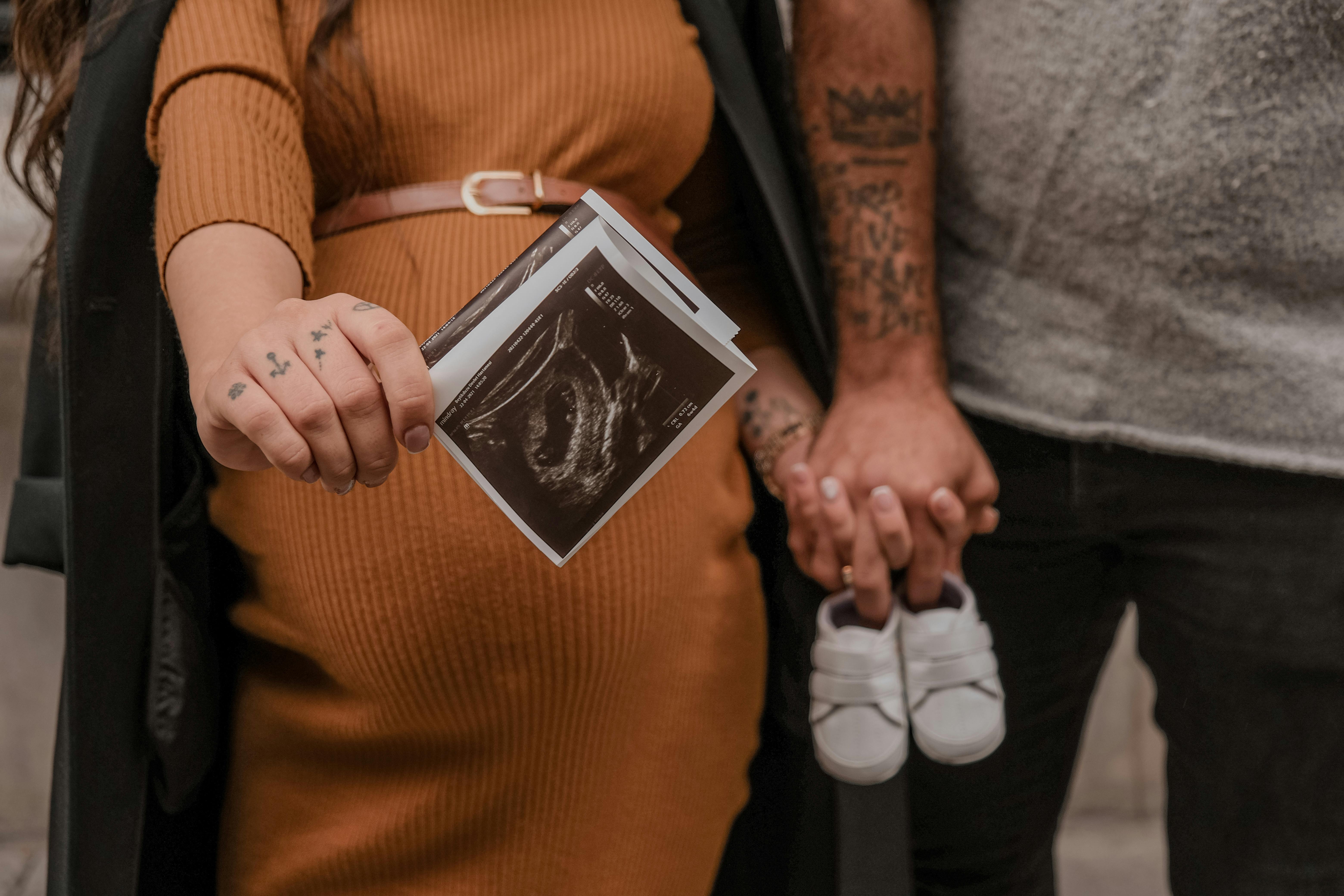 couple holding an ultrasound result and baby shoes