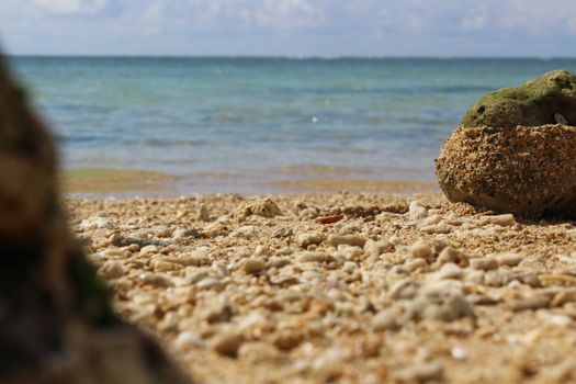 Detailed close-up of a rocky beach with focus on stones, sea waves in the background under a clear sky.