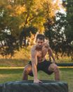 A Shirtless Male Exercising with Big Tier in a Park During Autumn
