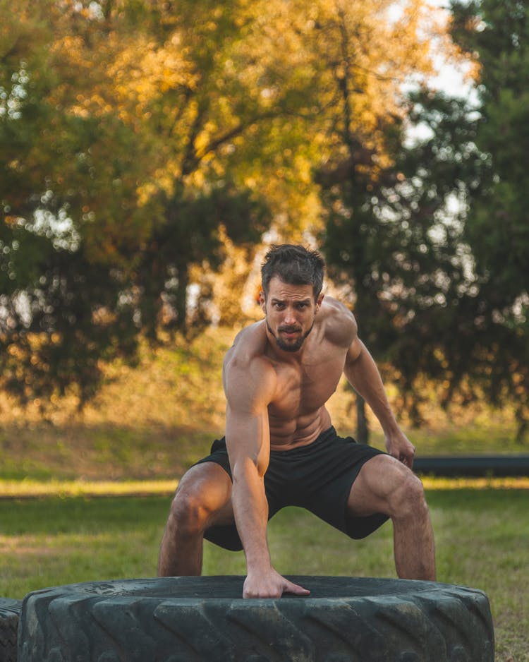 A Shirtless Male Exercising With Big Tier In A Park During Autumn 