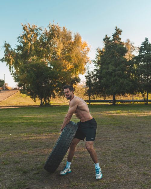 Free Muscular man flipping a tire on a grassy field, showcasing fitness and healthy living. Stock Photo