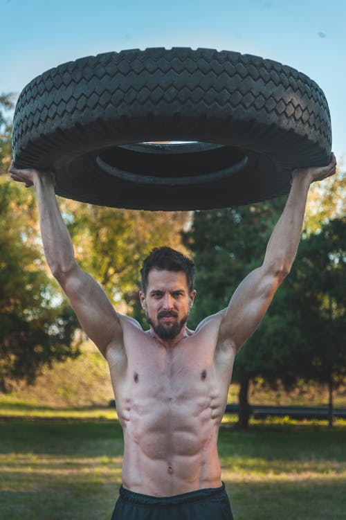 Topless Man Carrying a Large Tire