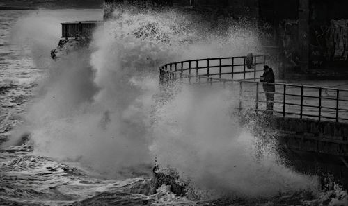Free Powerful ocean wave crashes against a pier, capturing the dramatic force of nature in a striking black and white image. Stock Photo