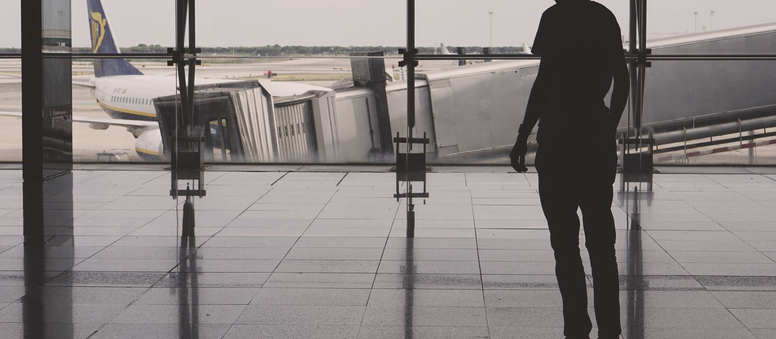 Silhouette of a man at El Prat airport with airplane reflections on glass walls.