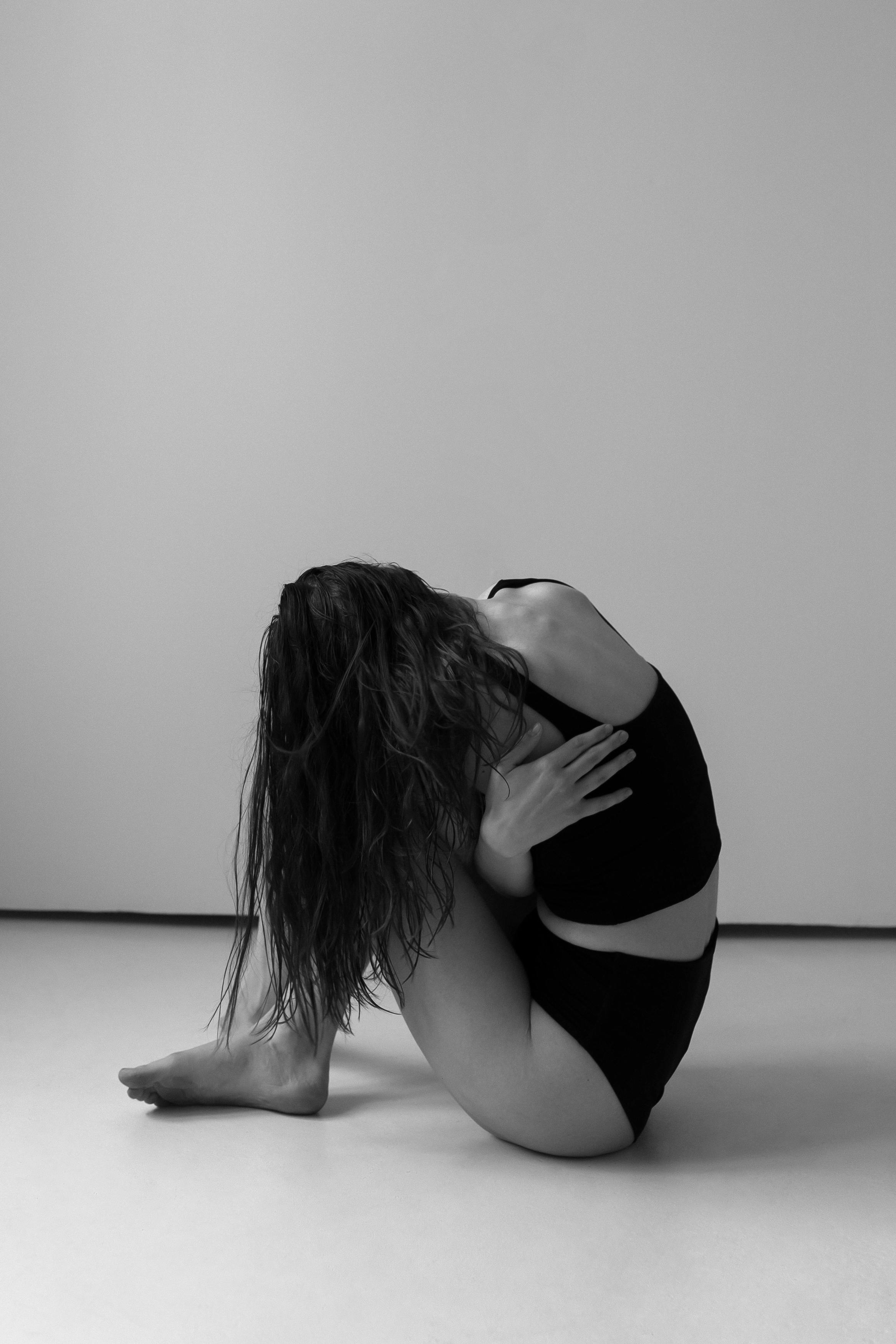 side view shot of a woman sitting on the floor while hugging herself