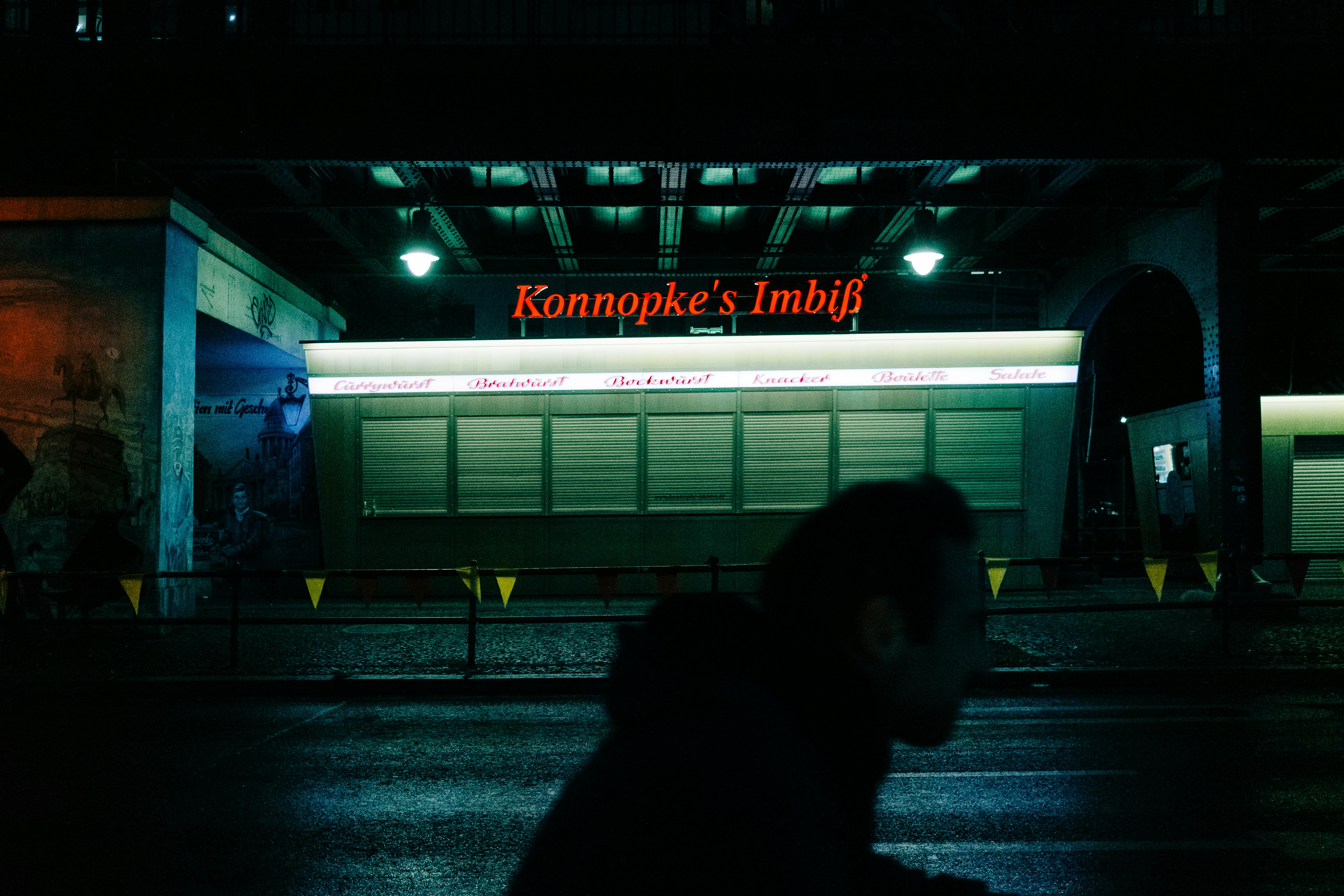 Mysterious night view of Konnopke's Imbiss in Berlin with silhouette foreground.