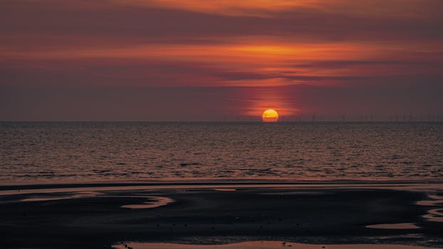 Stunning sunset over a tranquil beach with rippling water reflections in the foreground.