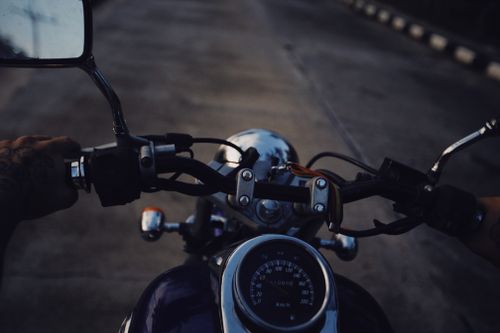Free Close-up shot of a motorcycle being ridden on a road at dusk, showcasing hands on handlebars and speedometer. Stock Photo