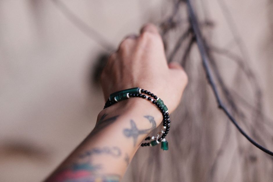 A tattooed hand wearing beaded bracelets reaching up, conveying a sense of style and personality.