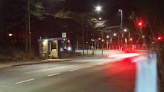 一条安静的夜间城市街道上，设有公交车站和路灯，过往汽车的车灯划出条条光带