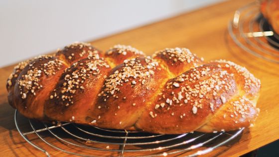 Glossy golden braided loaf crusted with pearl sugar cooling on a round wire rack