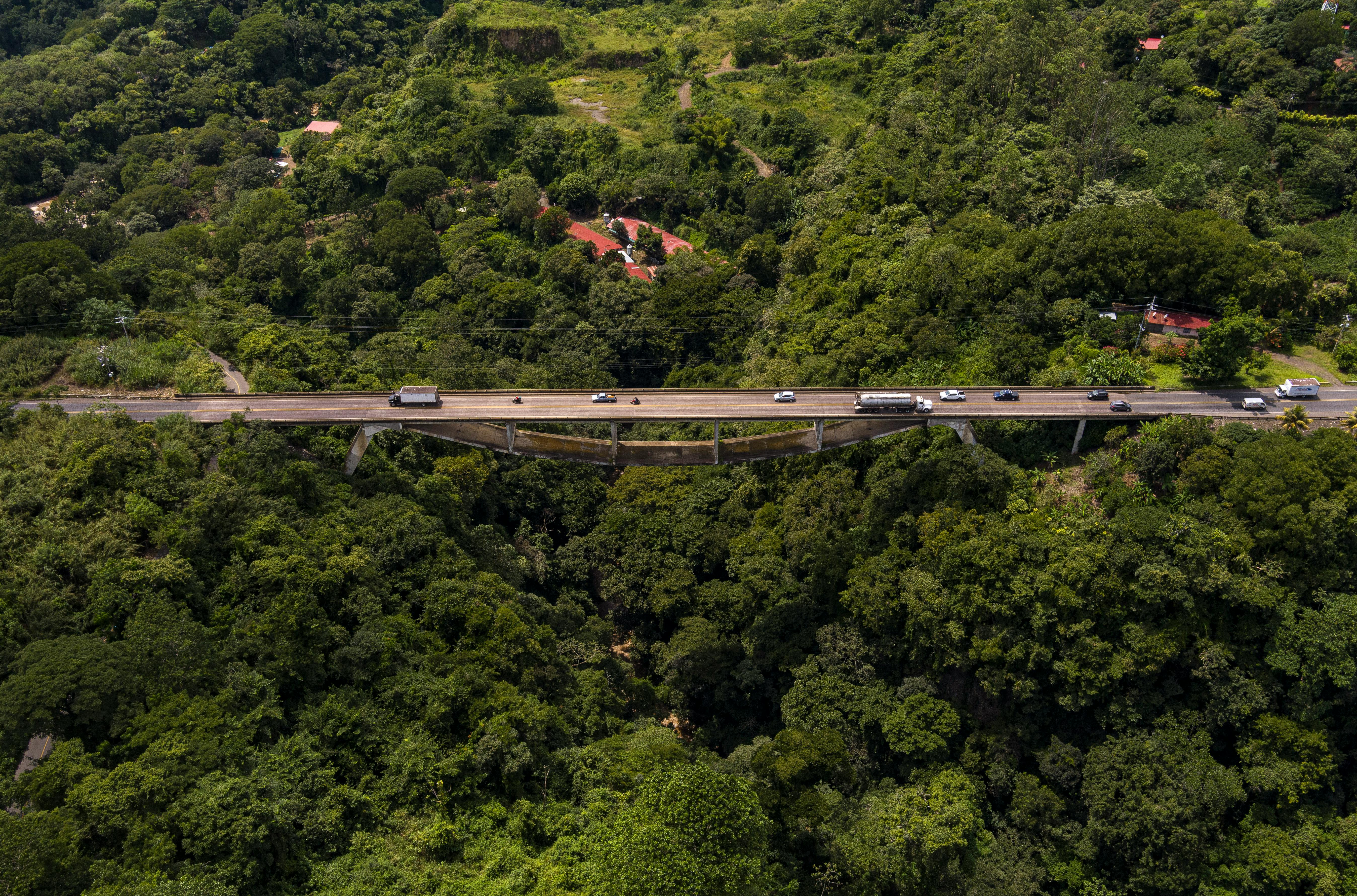 Aerial shot of a bridge and road cutting through dense forest in Grecia, Costa Rica.