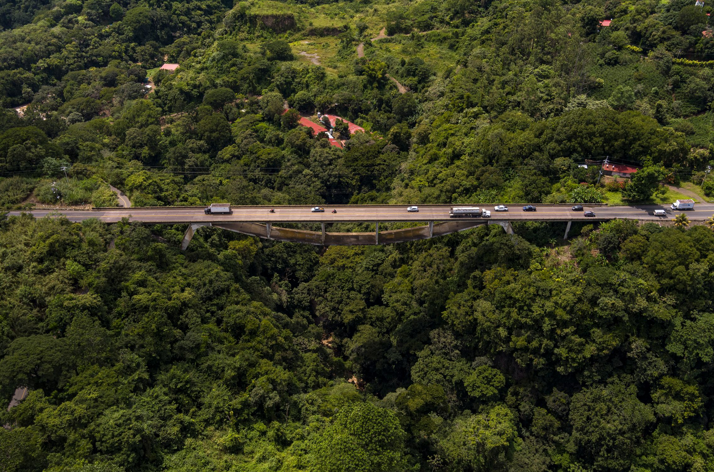 Aerial shot of a bridge and road cutting through dense forest in Grecia, Costa Rica