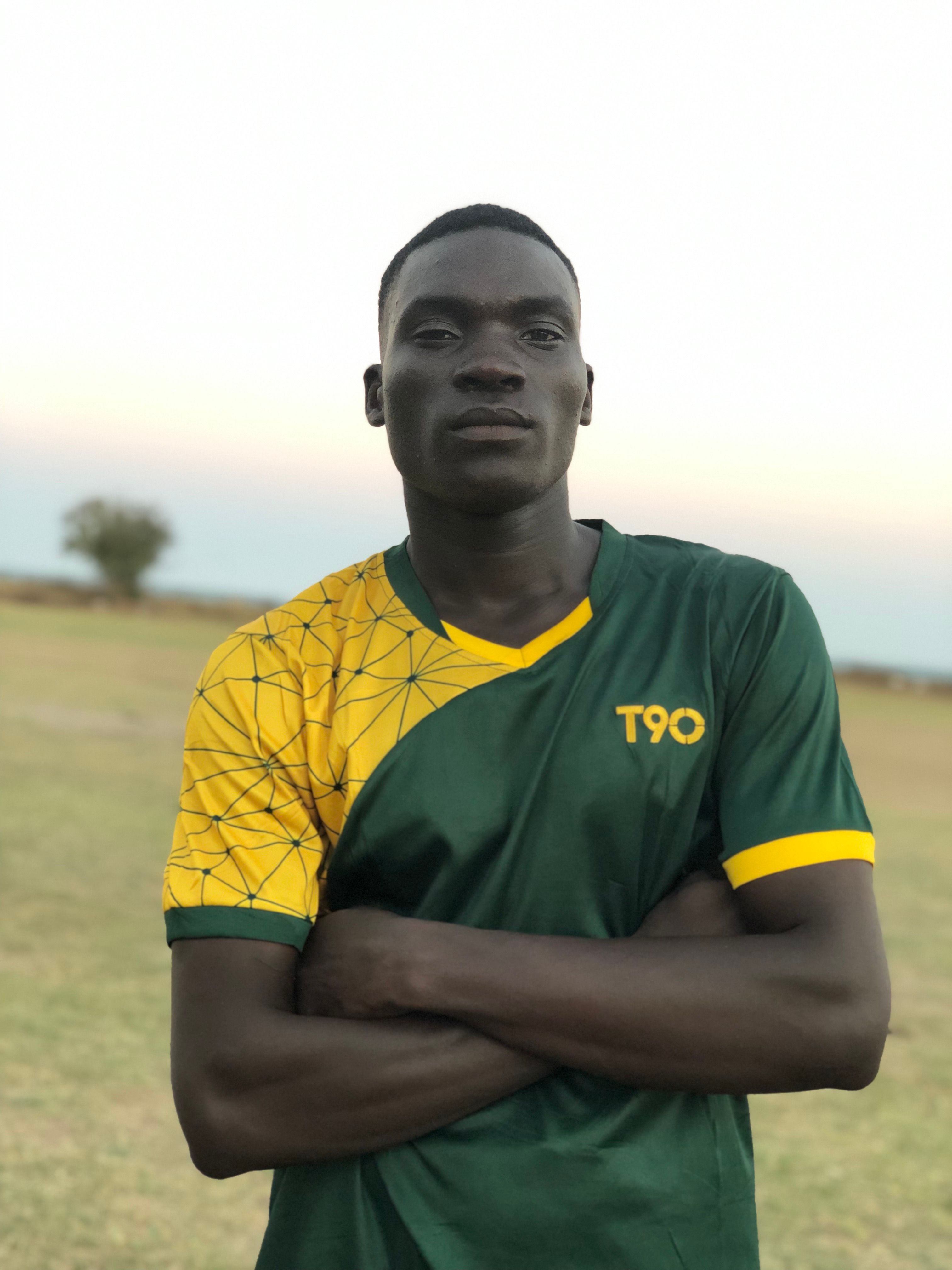 Confident young man standing outdoors in a green and yellow sports shirt with arms crossed.