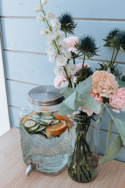 Free Elegant beverage jar with citrus slices and a floral bouquet on a wooden table. Stock Photo