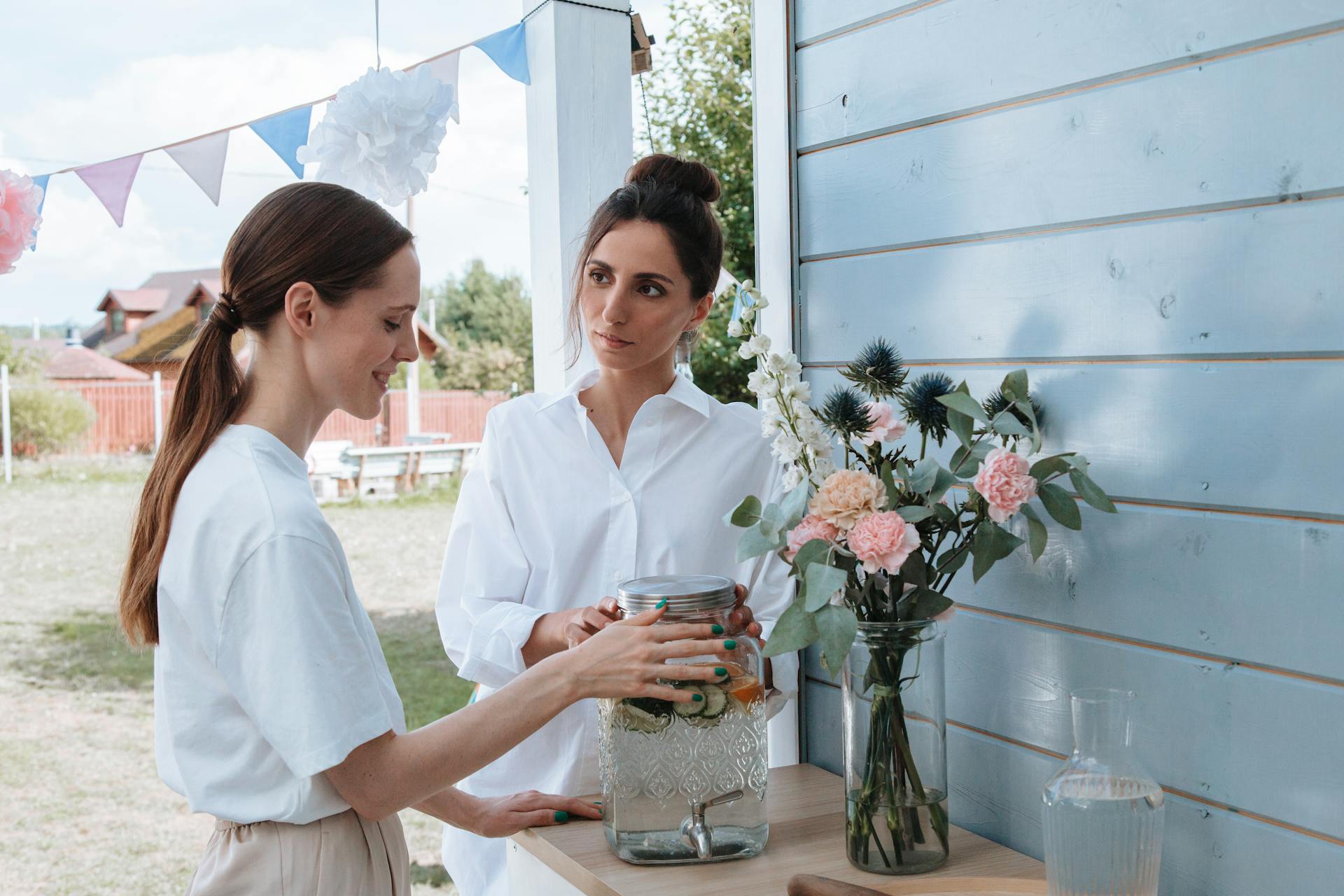 Two women enjoying a summer garden party with lemonade and floral decorations.