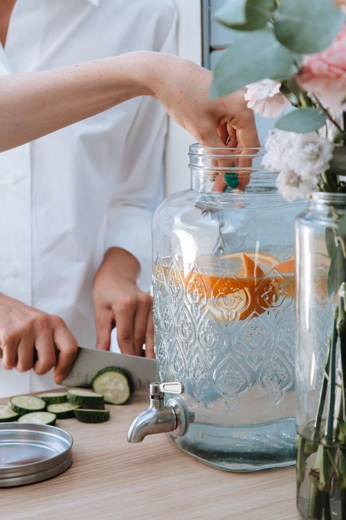 Free Two people preparing cucumber and citrus infused water in a glass dispenser. Stock Photo