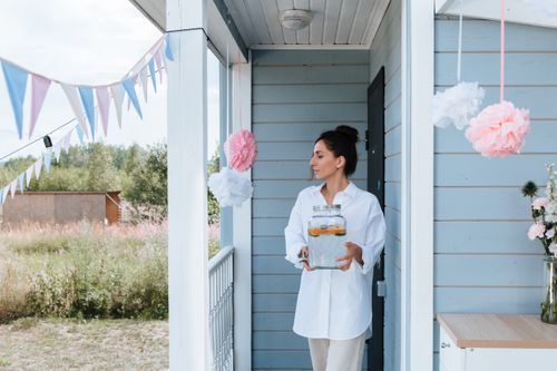 Free Woman holding lemonade jar at decorated house entrance for a summer party. Stock Photo