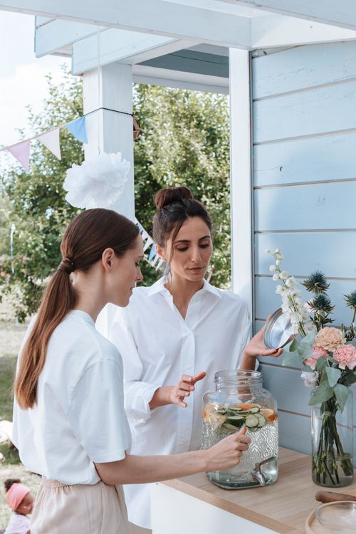 Free Two women prepare a refreshing lemon and cucumber infused water for an outdoor party setting. Stock Photo