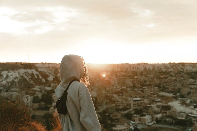 Woman In Hoodie On Hill Watching City In Sunset